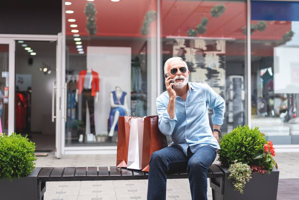 Senior man talking on mobile phone after shopping in city, consumerism concept  - Photo, image