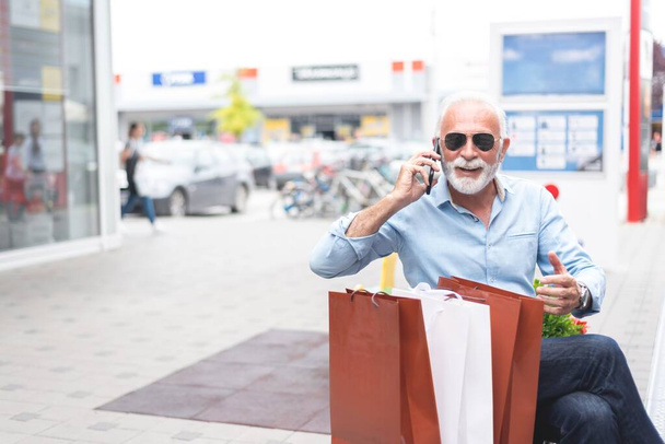Senior man talking on mobile phone after shopping in city, consumerism concept  - Foto, afbeelding