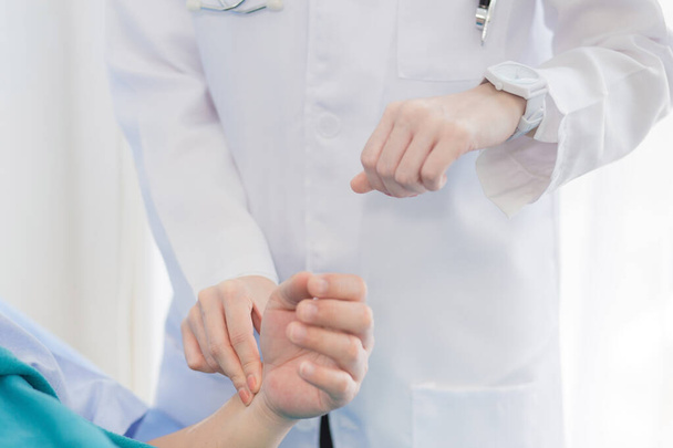 Una doctora está tomando el pulso en la muñeca de un paciente masculino para comprobar la frecuencia cardíaca en el hospital..  - Foto, imagen