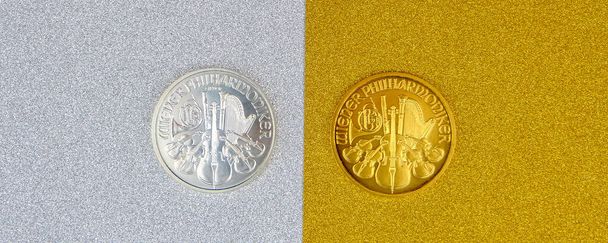 silver and golden austrian mint phillharmoniker one ounce coins laying on silver and golden background, image split in two halves - Photo, Image