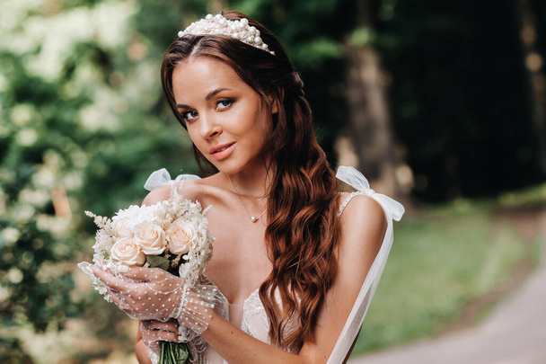 portrait of an elegant bride in a white dress with a bouquet in nature in a nature Park.Model in a wedding dress and gloves and with a bouquet .Belarus. - Fotoğraf, Görsel