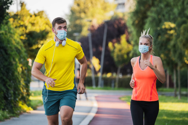 Young couple is jogging with protective masks. Covid-19 responsible behavior. - 写真・画像