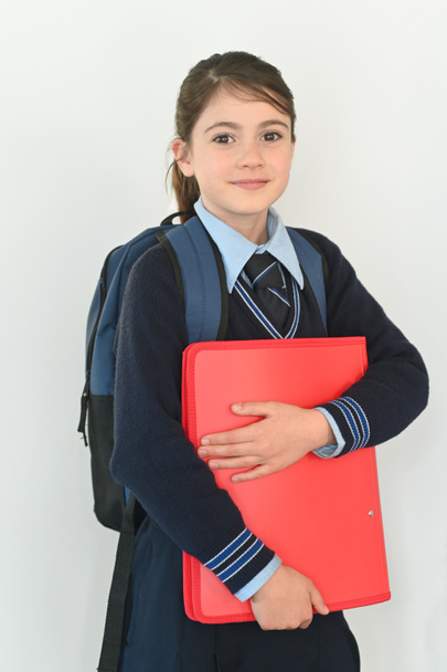 Junge Schülerin (10 Jahre) in Schuluniform trägt Schultasche und ein Ordner steht bereit für den Schulbesuch. - Foto, Bild