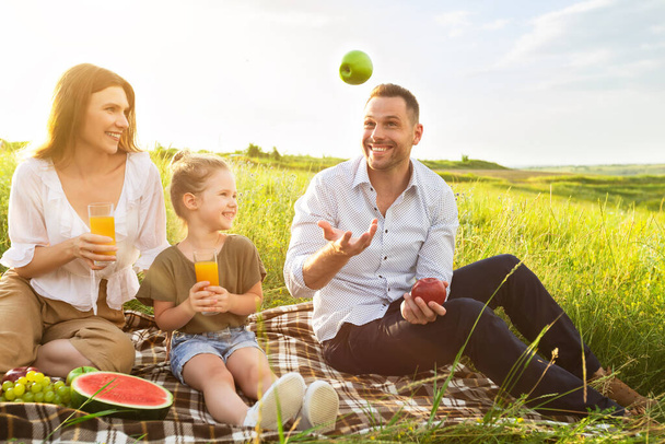 Feliz papá haciendo malabares con manzanas en un picnic afuera - Foto, imagen