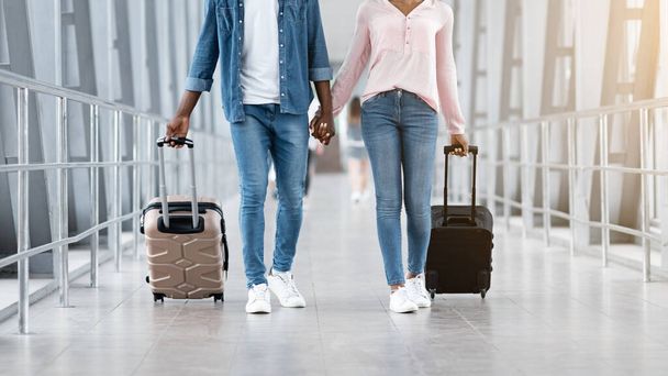 一緒に旅行する。空港ターミナルでスーツケースと黒のカップルウォーキング、手を握る - 写真・画像