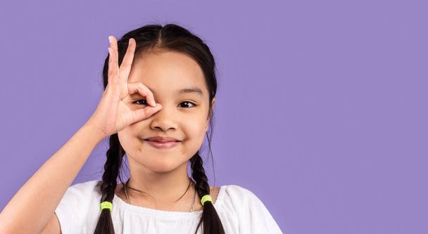 Aasialainen tyttö kattaa silmän OK merkki poseeraus studiossa - Valokuva, kuva