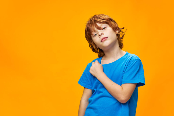 Beautiful red-haired boy in a blue t-shirt sad look yellow background - Fotografie, Obrázek