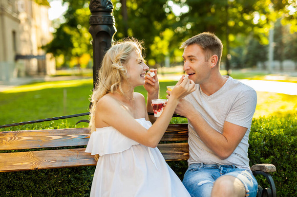 beautiful young couple expecting a baby are siting on a bench and eating ice-cream on the street - Foto, Imagem