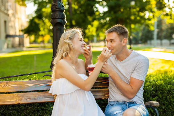 beautiful young couple expecting a baby are siting on a bench and eating ice-cream on the street - Valokuva, kuva