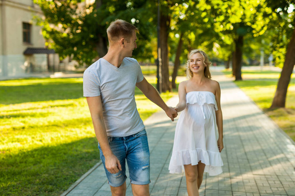 happy young pregnant woman with her husband walking in a city park - Valokuva, kuva
