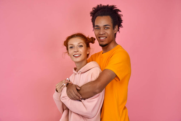 Smiling young couple in bright clothes fit isolated on pink background in studio - Fotó, kép