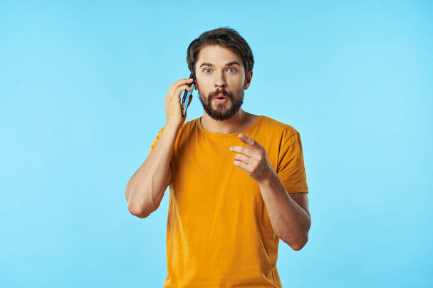  mobile phone in the hand of a man in a yellow T-shirt - Photo, Image