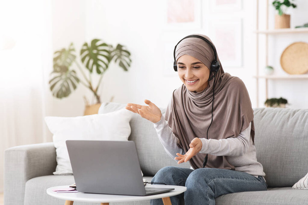 Онлайн деловая встреча. Арабская женщина использует гарнитуру и ноутбук для видеоконференции - Фото, изображение