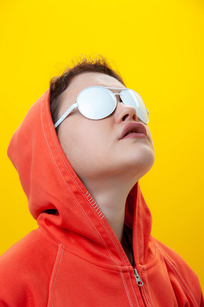 Close up fashion portrait young beautiful woman in hoodie and white glasses. Alternative funky girl on a bright yellow background. Unusual youth fashion concept. Hot image. - Foto, afbeelding