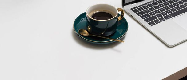 Закрыть вид на рабочее пространство зеленой керамической чашкой кофе, ноутбуком и копировальным пространством на белом столе - Фото, изображение