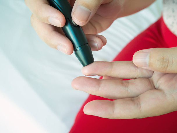 woman using lancelet on finger, diabetes test checking blood sugar level - Foto, imagen