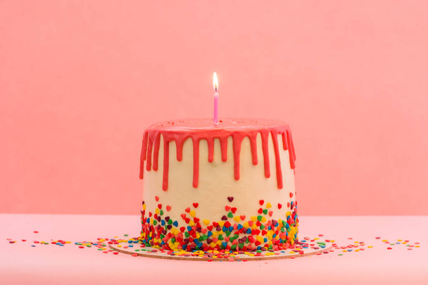 Grote taart met één kaars. Gelukkige verjaardagskaarsen. Taart met rode chocolade decoratie op roze achtergrond. Heldere kaarsen. Gelukkige verjaardag. Zoet en smakelijk dessert. - Foto, afbeelding