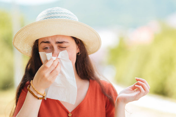 藁帽子の女性がハンカチで鼻を吹く。コピースペース。屋外だ。アレルギーとウイルスの概念. - 写真・画像