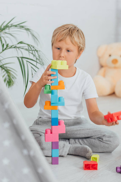 enfoque selectivo de niño en pijama sentado en el suelo y jugando con bloques de construcción multicolores - Foto, Imagen