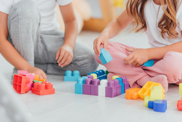 cropped view of children playing with building blocks while sitting on floor in pajamas - Valokuva, kuva