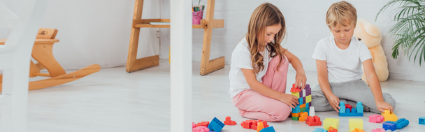 concept horizontal de sœur et frère en pyjama assis sur le sol et jouer avec les blocs de construction - Photo, image