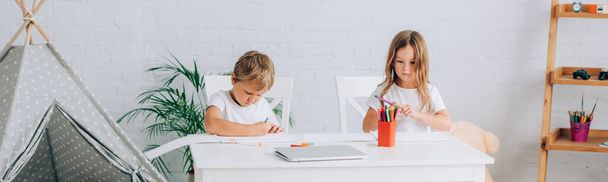 image horizontale du frère et de la sœur en pyjama dessin avec des stylos en feutre à table près des enfants wigwam - Photo, image