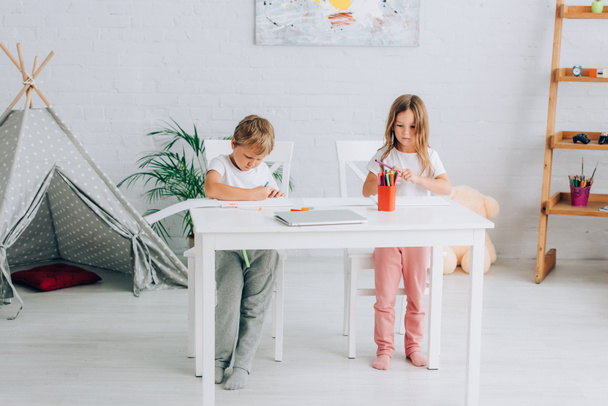 パジャマの兄と妹は子供の近くのテーブルでフェルトペンで絵を描いています - 写真・画像