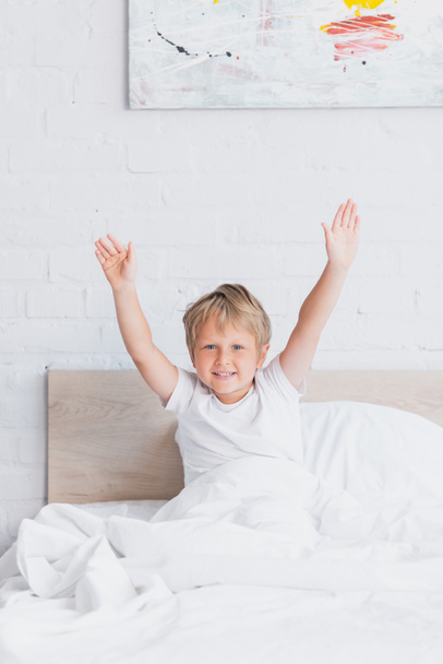 awakened boy in white t-shirt stretching while sitting in bed - Foto, imagen