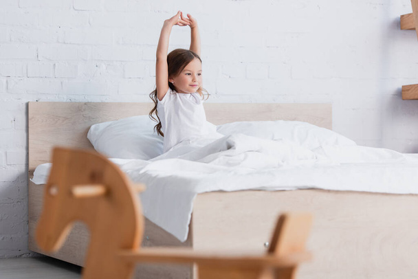 selective focus of awakened kid stretching while sitting in bed - Photo, Image