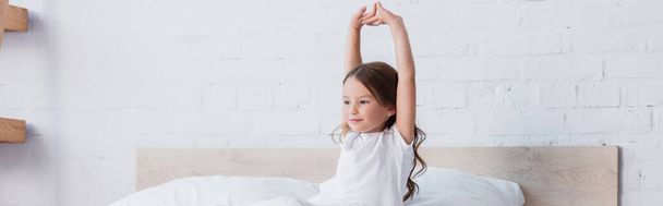 panoramic shot of awakened child stretching while sitting in bed  - 写真・画像