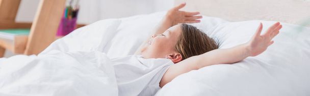 horizontales Bild eines erwachten Mädchens, das sich dehnt, während es im Bett liegt - Foto, Bild