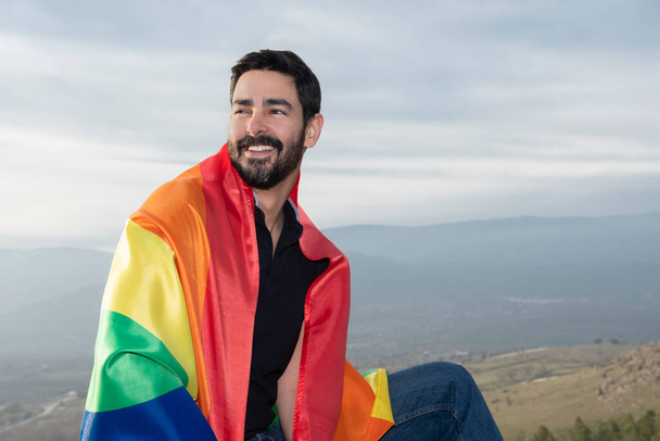 Homosexuell lachend mit einer schwulen Flagge am Horizont. Konzept von Homosexualität, Stolz, Vielfalt - Foto, Bild
