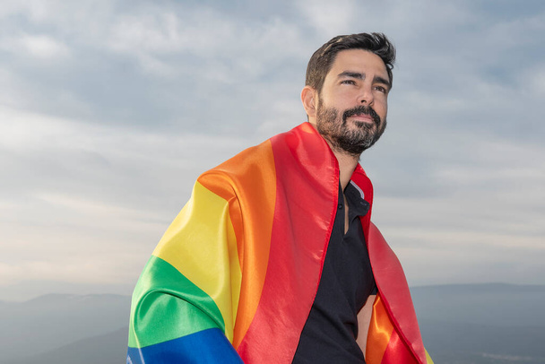 Homosexuell lachend mit einer schwulen Fahne am Horizont sitzend. Konzept von Homosexualität, Stolz, Vielfalt - Foto, Bild
