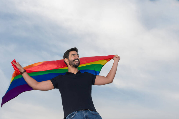青い空の地平線を見て座っているゲイの旗で立って笑っている男の子。ゲイプライド多様性という概念は - 写真・画像