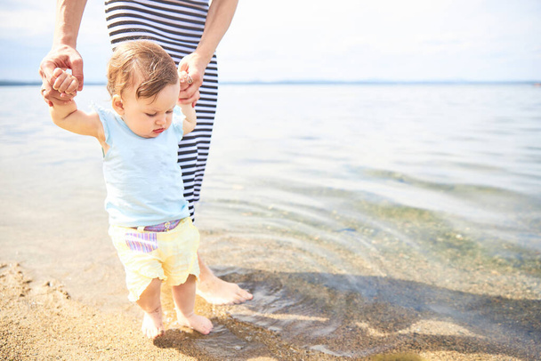 Mom learns to walk little baby on the sand at the beach - Foto, Bild