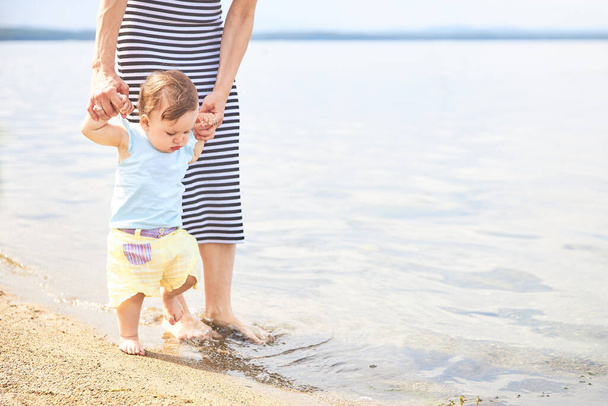Mom learns to walk little baby on the sand at the beach - Photo, Image