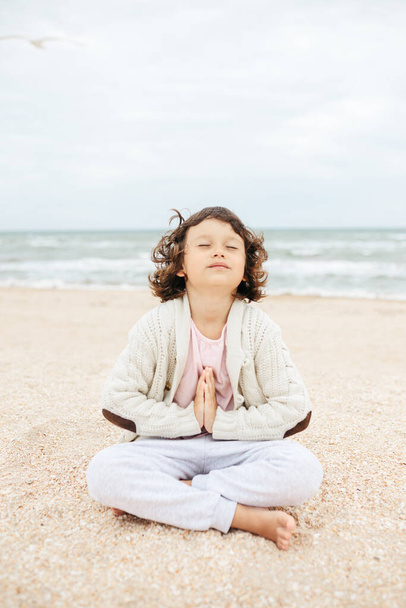 little girl meditating on the beach, doing yoga, pastel colors - 写真・画像