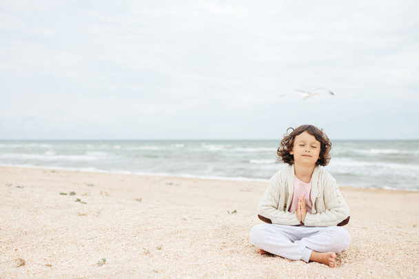 маленькая девочка медитирует на пляже, занимается йогой, пастельными красками - Фото, изображение