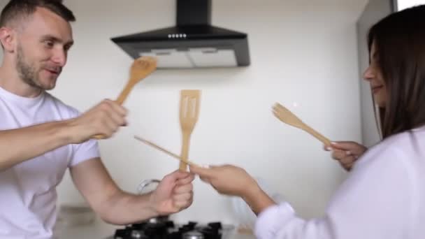 Young couple fights with wooden spoons in the kitchen. Morning fun at home - Footage, Video