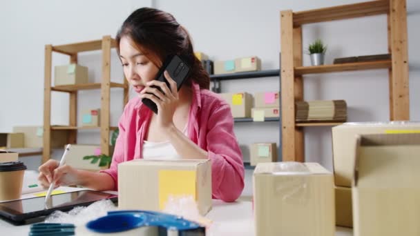 Young Asia businesswoman using mobile phone call receiving purchase order and check product on stock, work at home office. Small business owner, online market delivery, lifestyle freelance concept. - Footage, Video