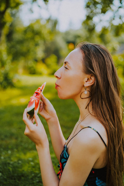 beautiful young woman with long hair, lies on the lawn with a slice of watermelon. Woman eating ripe watermelon in nature. - Foto, Imagem