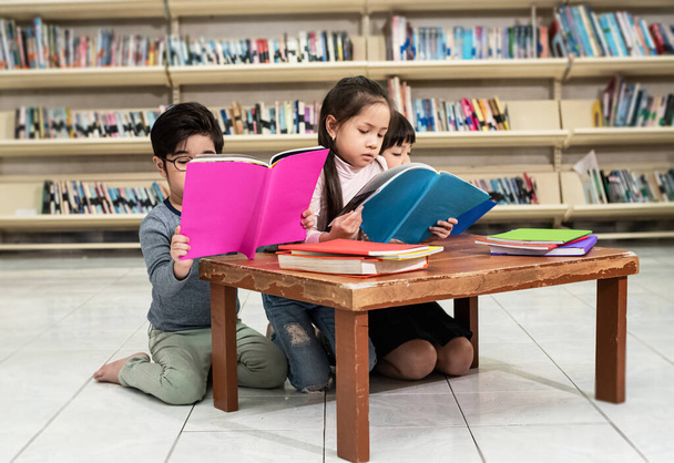 Τρία παιδιά διαβάζουν βιβλία μαζί στο σχολείο, με ενδιαφέρον συναίσθημα, θολό φως γύρω - Φωτογραφία, εικόνα