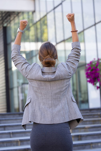 Takanäkymä houkutteleva liiketoiminnan nainen nosti kädet seisoo edessä toimistorakennus ja juhlii menestystä - Valokuva, kuva