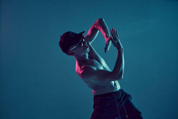 Guy breakdancer in cap and sunglasses dance hip-hop in neon blue light. Dance school poster - Fotoğraf, Görsel