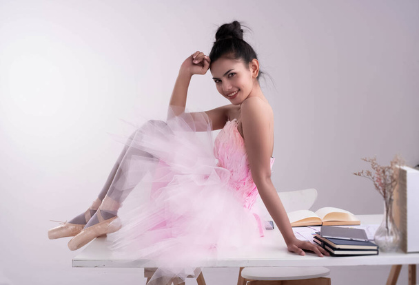 Joven hermosa dama con traje de ballet rosa sentado en el escritorio de madera, modelo de retrato posando - Foto, imagen