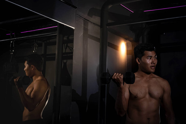 Handsome man raising dumbbell up and down,doing exercise for buit muscle,reflection in the mirror,fit and firm body - Fotografie, Obrázek
