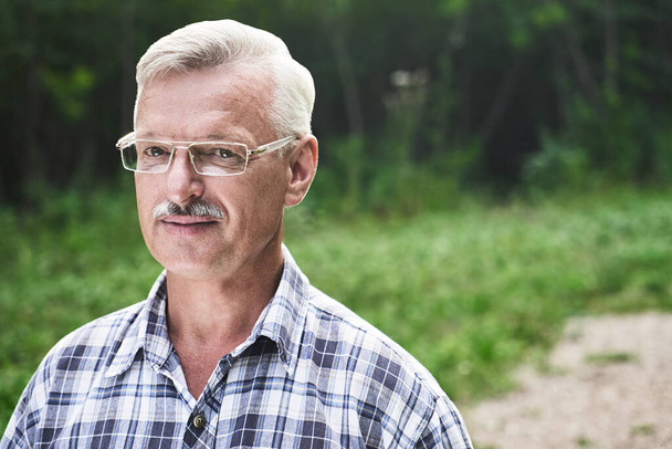 Close-up portrait of handsome gray-haired adult man with mustache and glasses smiling on the background of a summer forest park - Φωτογραφία, εικόνα