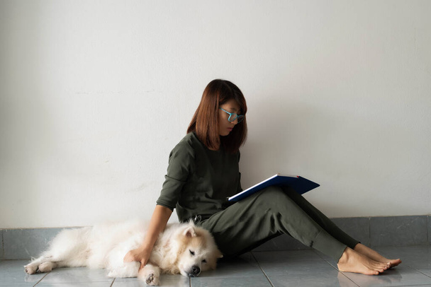 Señora sentada al lado de su perro y leyendo el libro, relajarse tiempo en casa - Foto, Imagen