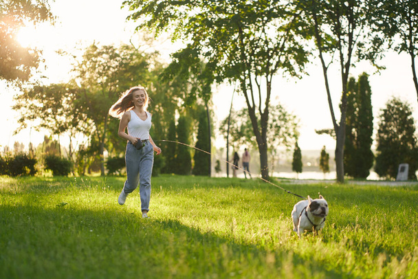 Laughing woman running with french bulldog in park. - 写真・画像