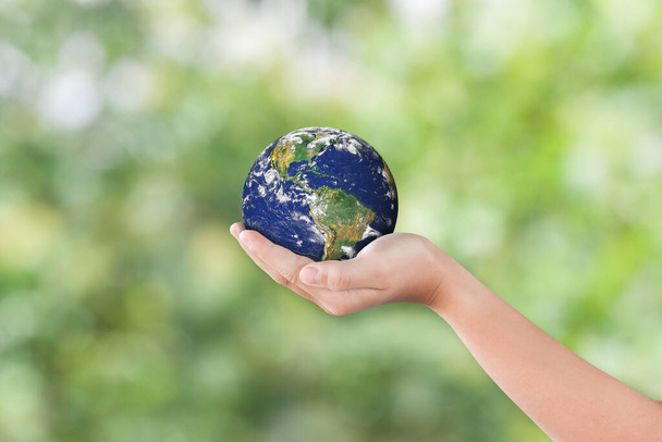 Koncepcja dnia środowiska: Ręce dziecka trzymające ziemię nad rozmazanym zielonym tle natury. Elementy tego obrazu dostarczone przez NASA - Zdjęcie, obraz